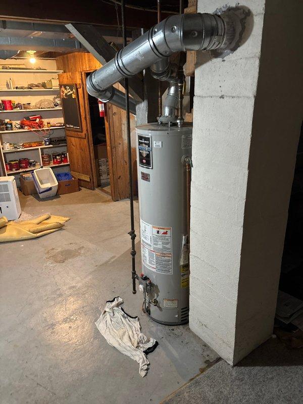 Responded to water heater leaking from base. Upon inspection, confirmed active leak originating from the bottom of the unit, indicating internal tank failure. Explained to customer that leaks from the base typically result from sediment buildup and corrosion over time, which compromises tank integrity and cannot be repaired. Recommended full water heater replacement as the only viable solution. Customer approved replacement. Shut off water supply and gas line to existing unit, drained tank completely, and disconnected all water lines, gas connections, and venting system. Removed failed water heater from basement mechanical room. Installed new white cylindrical water heater in same location against wall. Connected cold water inlet and hot water outlet lines to top of unit using appropriate fittings. Reconnected gas supply line with black pipe and verified all connections for proper seal. Installed metallic ductwork and flexible corrugated venting to exhaust combustion gases safely throu
