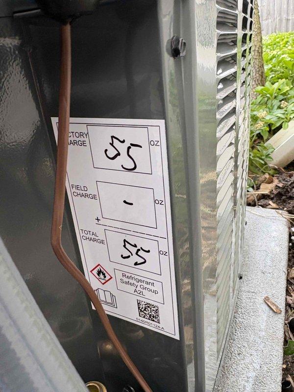 Completed full air conditioning system installation including outdoor condenser unit positioned on concrete pad with proper clearances from structure. Installed refrigerant lines, electrical disconnect box, and flexible conduit routing from unit to building exterior. System charged with refrigerant to manufacturer specifications, documented refrigerant levels at 55/55 on service label, and verified all electrical connections secure and operational.