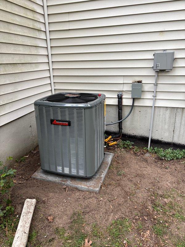 Completed full HVAC system installation including new Amana air conditioning condenser unit and furnace. Outdoor condenser positioned on concrete pad against exterior wall with proper electrical disconnect box, refrigerant line installation, and secure mounting of all components. Indoor furnace installed in basement mechanical room with complete ductwork connections, proper ventilation, and integration with existing distribution system.