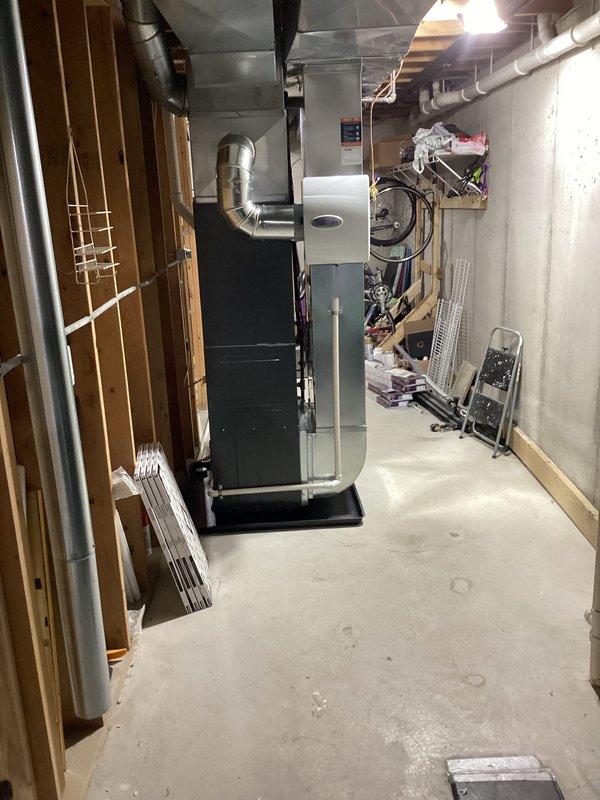 Completed full HVAC system installation including new Amana air conditioning condenser unit and furnace. Outdoor condenser positioned on concrete pad against exterior wall with proper electrical disconnect box, refrigerant line installation, and secure mounting of all components. Indoor furnace installed in basement mechanical room with complete ductwork connections, proper ventilation, and integration with existing distribution system.