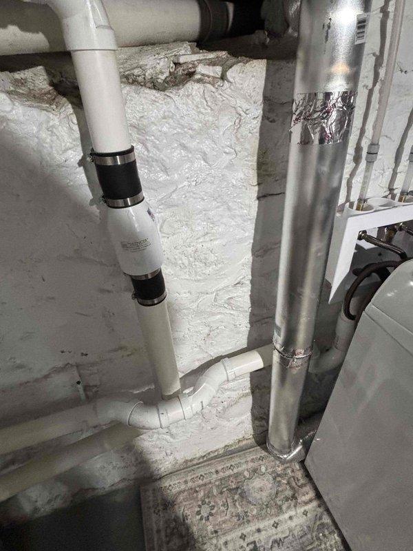 # Laundry Room Plumbing Rework

Completed comprehensive plumbing system rework in basement utility area. Reconfigured white PVC drainage piping with new vertical and horizontal runs, installed black coupling connectors, and secured all lines with proper metal clamps at appropriate intervals. Performed diagnostic testing of water heater/boiler unit and verified all connections for proper drainage flow and system integrity.