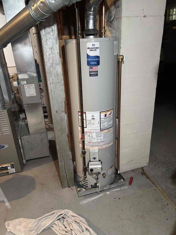 Successfully installed a Bradford White residential water heater in basement utility area. Connected copper supply and discharge piping with proper fittings and valves, installed vent piping, and verified all connections for proper operation. Unit tested and confirmed operational with all safety labels and specifications visible and compliant.