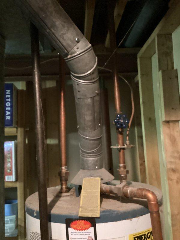 Completed estimate for water heater replacement in residential basement. Assessed existing white cylindrical water heater with connected copper supply and discharge piping, blue valve assembly, and metal exhaust vent system showing signs of age and deterioration. Documented current installation configuration including pipe routing, venting arrangement, and clearance requirements for replacement unit recommendation.
