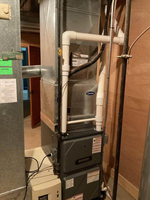 Responded to service call for air conditioning system not cooling with suspected refrigerant leak. Upon arrival, inspected 22-year-old Carrier air handler unit and associated HVAC equipment located in basement utility area. Visual assessment revealed aging system with significant rust and weathering on furnace casing, copper refrigerant lines, and connected ductwork. Documented existing equipment configuration including air handler, furnace unit, PVC condensate drainage, electrical connections, and refrigerant line routing for estimate preparation. Photographed installation to support diagnostic findings and provide visual reference for recommended repairs or replacement options.