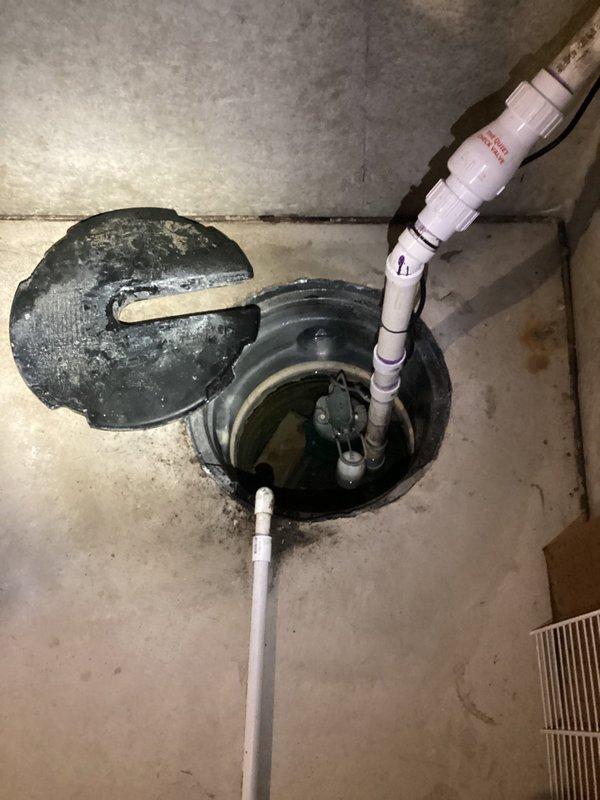 Responded to service call for non-heating water heater and sump pump spraying water onto basement floor. Upon inspection, found 4-year-old water heater with no hot water production and active sump pump discharge issue causing water spillage. Assessed water heater components, PVC discharge piping configuration, and sump pump basin assembly. Documented equipment conditions including water heater tank, copper and PVC supply lines, pump mechanism submerged in basin, and concrete floor water damage from sump discharge malfunction.