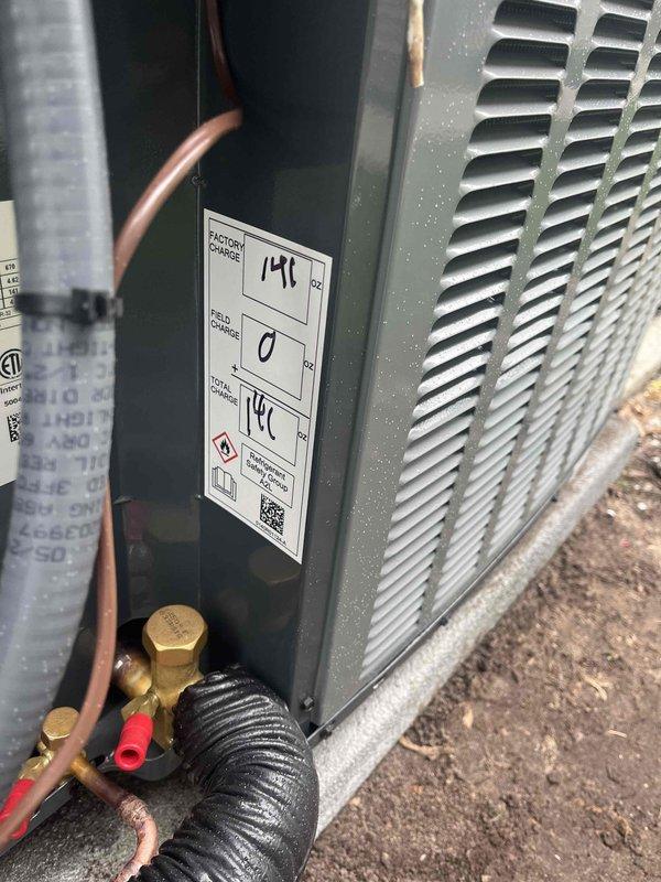 Completed installation of new outdoor HVAC condensing unit at residential property. Unit was properly positioned on concrete pad, with refrigerant lines connected and secured using brass service valves and fittings. Copper line sets were insulated with black ribbed insulation, and all connections were tightened to manufacturer specifications. Electrical conduit was run vertically along exterior wall to provide power supply to the unit. System was charged with refrigerant, pressure tested, and verified operational. Service ports were capped, and unit was labeled with installation data including refrigerant charge information. Second existing unit remains in operation alongside new installation, both positioned on separate concrete pads against home's exterior siding. All work completed per industry standards and manufacturer guidelines.