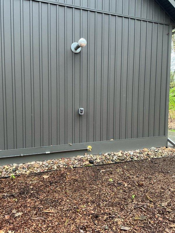 Completed estimate for mini split system installation to provide climate control for small room space. Evaluated exterior wall location on gray metal siding for potential outdoor condenser unit placement, noting existing PVC pipe penetrations and utility box that will need to be considered during installation planning. Assessed attic space for indoor air handler installation, confirming adequate structural support from exposed roof trusses and sufficient clearance for equipment mounting and refrigerant line routing. Documented current construction status of partially finished drywall and concrete flooring to coordinate mini split installation with ongoing renovation work. Provided recommendations for equipment sizing and placement to optimize heating and cooling efficiency for the conditioned space.
