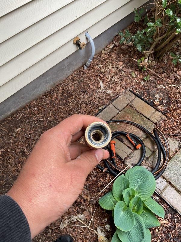 Replaced defective exterior hose bib on building with white lap siding. Removed old brass-colored spigot valve and galvanized curved pipe section that had failed, installed new functioning outdoor faucet assembly with proper threading and secure wall mounting to restore water access to exterior of property.