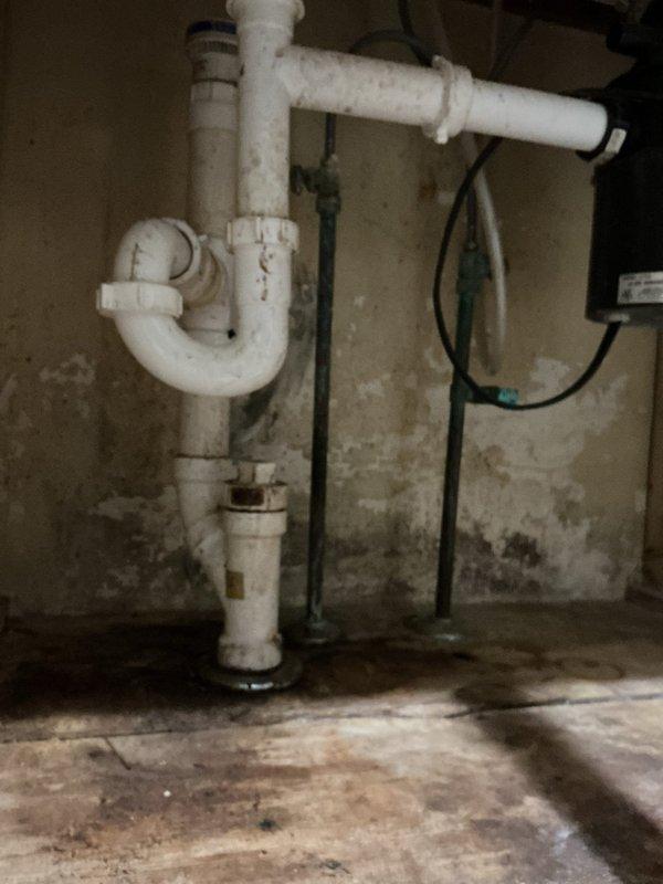Responded to clogged sink drain issue where previous snaking attempts were unsuccessful. Upon arrival, accessed plumbing system through side entrance and inspected the drain assembly. Located white PVC P-trap configuration in basement utility area showing significant age and wear with rust staining at metal-to-PVC connections. Performed thorough drain clearing procedure using professional equipment to remove stubborn blockage that standard snake could not reach. Tested drainage flow to confirm proper operation and verified complete clearance of obstruction. Documented existing conditions including aged plumbing components, moisture staining on surrounding surfaces, and general wear on drain assembly for customer records.