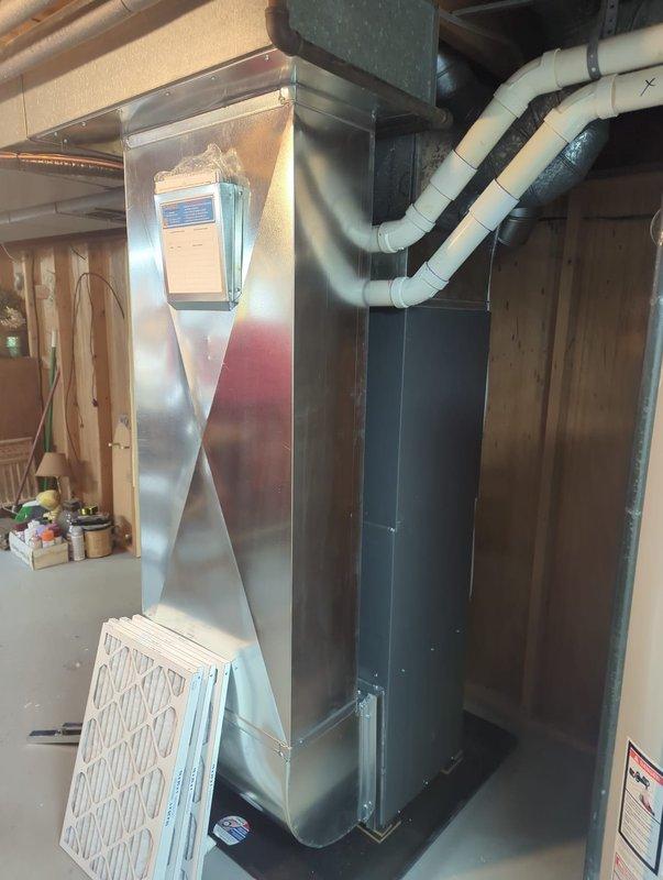 Completed full HVAC system installation in basement utility area, including new furnace unit with air handler and add-on air conditioning system. Installed white PVC condensate drainage and venting piping with proper securing straps, connected black flexible ductwork to sheet metal plenum, and mounted all equipment on protective drip pan platform. System includes integrated humidifier accessory, fresh air filtration components, and complete duct transitions for proper airflow distribution throughout the residence.