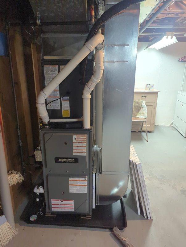 Completed full HVAC system installation in basement utility area, including new furnace unit with air handler and add-on air conditioning system. Installed white PVC condensate drainage and venting piping with proper securing straps, connected black flexible ductwork to sheet metal plenum, and mounted all equipment on protective drip pan platform. System includes integrated humidifier accessory, fresh air filtration components, and complete duct transitions for proper airflow distribution throughout the residence.