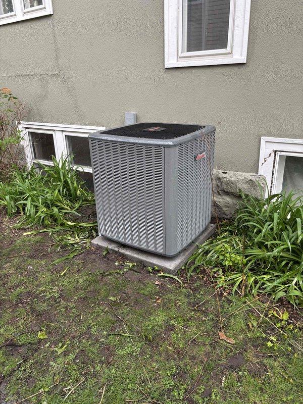 Completed full air conditioning system replacement at residential property. Removed existing outdoor condenser unit and installed new gray HVAC condenser on concrete pad against exterior wall with beige stucco siding. Unit positioned with proper clearance from foundation and windows for adequate airflow and service access. Secured electrical connections via conduit running from wall-mounted disconnect box to condensing unit. Verified unit is level on pad and properly anchored. Tested system operation and confirmed proper refrigerant charge and electrical connections. Work site cleaned and unit operational upon completion.