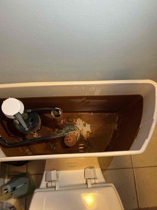 Responded to service call for leaking toilet with broken valve in home rebuilt around 2000. Upon inspection, removed tank lid and identified severely corroded fill valve assembly with compromised internal components, evidenced by brown discolored water indicating significant rust and mineral buildup throughout tank. Replaced faulty fill valve assembly with new unit, flushed system multiple times to clear sediment, and tested for proper operation and leak elimination. Verified no water leakage after restoration of water supply and confirmed all tank components functioning correctly.