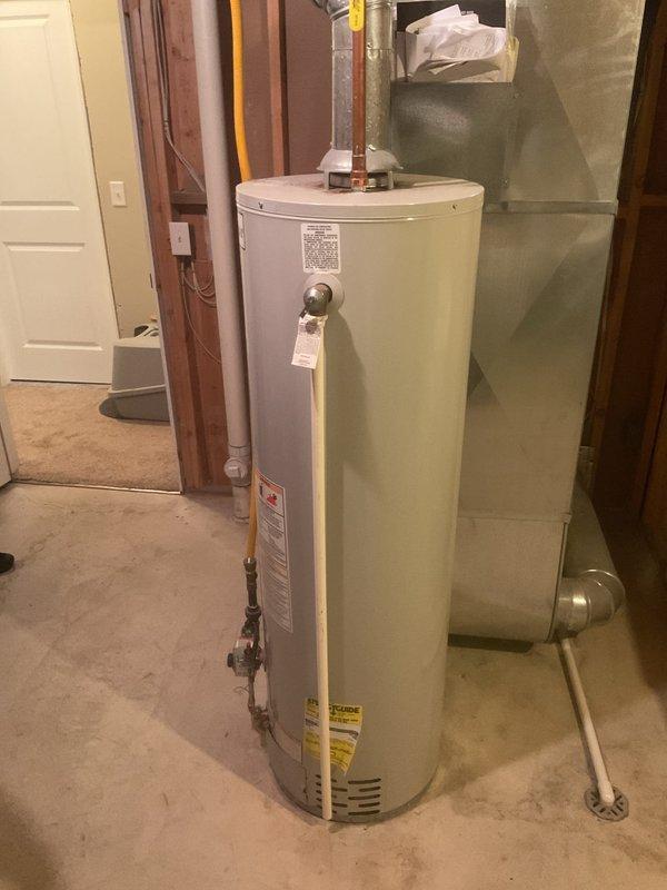 Provided estimate for water heater replacement in residential utility room. Assessed existing white cylindrical water heater installation with standard plumbing connections, copper piping, and PVC venting system. Documented current equipment condition, surrounding HVAC infrastructure including green furnace unit, and existing ductwork configuration to prepare comprehensive replacement proposal.