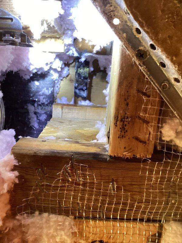 Responded to boiler water return line leak. Upon arrival, accessed attic space to locate source of leak in heating system piping. Inspected return line routing through insulated attic area and identified active leak point. Documented conditions with photographs showing copper piping running through attic joists with surrounding fiberglass insulation. Assessed damaged screening and deteriorated wooden access frame requiring attention. Repaired leaking connection on return line and verified system integrity. Confirmed no further active leaks present and proper water flow restored to boiler system.