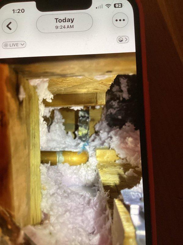 Responded to boiler water return line leak. Upon arrival, accessed attic space to locate source of leak in heating system piping. Inspected return line routing through insulated attic area and identified active leak point. Documented conditions with photographs showing copper piping running through attic joists with surrounding fiberglass insulation. Assessed damaged screening and deteriorated wooden access frame requiring attention. Repaired leaking connection on return line and verified system integrity. Confirmed no further active leaks present and proper water flow restored to boiler system.