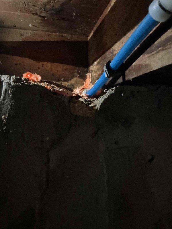 Responded to recurring exterior hose faucet leak spraying water behind siding when activated. Upon inspection, discovered severely corroded and deteriorated copper piping and fittings in crawl space serving the outdoor spigot, with extensive oxidation, rust buildup, and white mineral deposits indicating long-term moisture exposure. The compromised piping was causing water to spray behind the siding rather than through the faucet properly. Documented existing conditions showing failed previous repair attempts and structural water damage to surrounding wooden joists and beams. Photographed exterior utility area and interior crawl space deterioration for assessment. Advised on necessary copper pipe replacement and proper installation to resolve chronic leaking issue in this century-old renovated home.