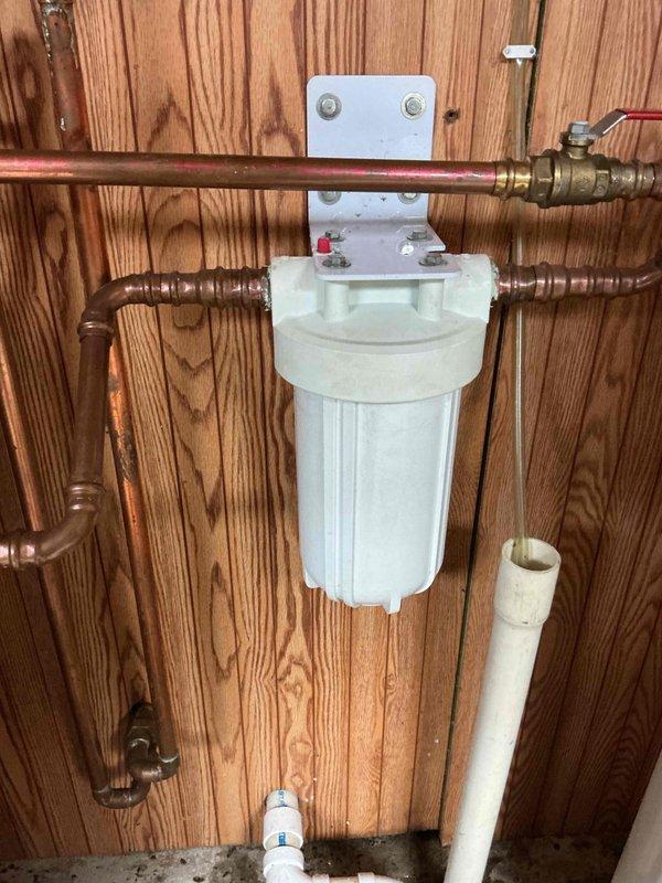 Replaced whole home water filter cartridge due to heavy sediment accumulation and discoloration. Removed old filter element from white cylindrical housing mounted to wooden wall panel, installed new replacement cartridge, and reassembled unit. Verified proper sealing of housing and checked for leaks at copper pipe connections and brass valve fittings. System restored to full operational status with clean filter media in place.