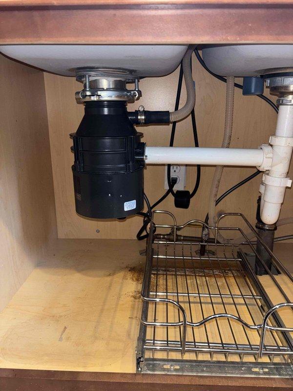 Responded to service call for leaking garbage disposal causing water damage in basement. Upon inspection, determined existing disposal unit had failed and required complete replacement. Removed defective garbage disposal unit and disconnected all associated plumbing connections and electrical supply. Installed new black garbage disposal unit with proper mounting assembly to stainless steel sink basin. Connected discharge plumbing to existing white PVC drain system with appropriate trap configuration. Wired electrical connection and verified proper operation. Tested unit under running water to confirm no leaks at mounting flange, discharge connections, or drain assembly. Disposal operating correctly with no further leakage detected.