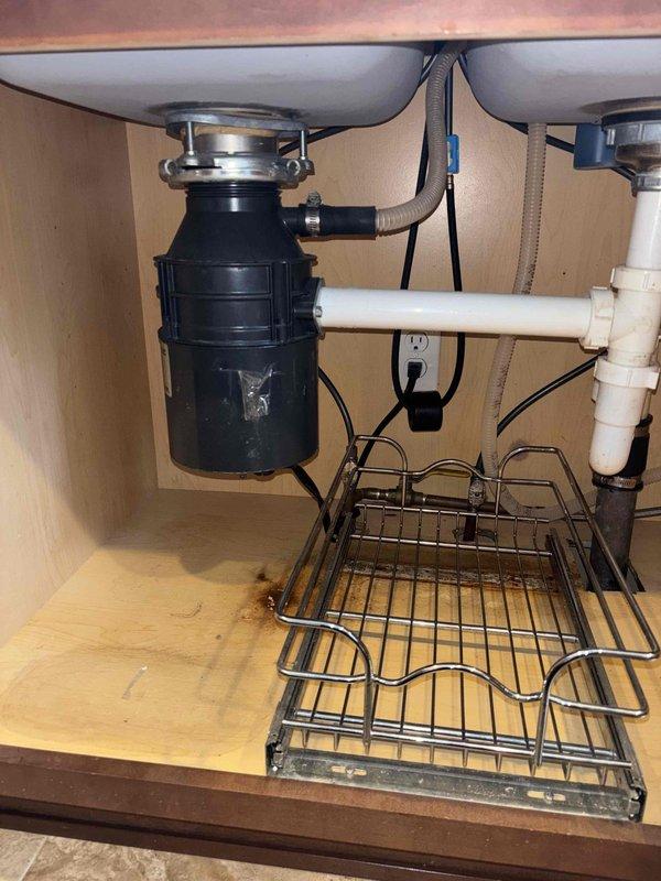 Responded to service call for leaking garbage disposal causing water damage in basement. Upon inspection, determined existing disposal unit had failed and required complete replacement. Removed defective garbage disposal unit and disconnected all associated plumbing connections and electrical supply. Installed new black garbage disposal unit with proper mounting assembly to stainless steel sink basin. Connected discharge plumbing to existing white PVC drain system with appropriate trap configuration. Wired electrical connection and verified proper operation. Tested unit under running water to confirm no leaks at mounting flange, discharge connections, or drain assembly. Disposal operating correctly with no further leakage detected.