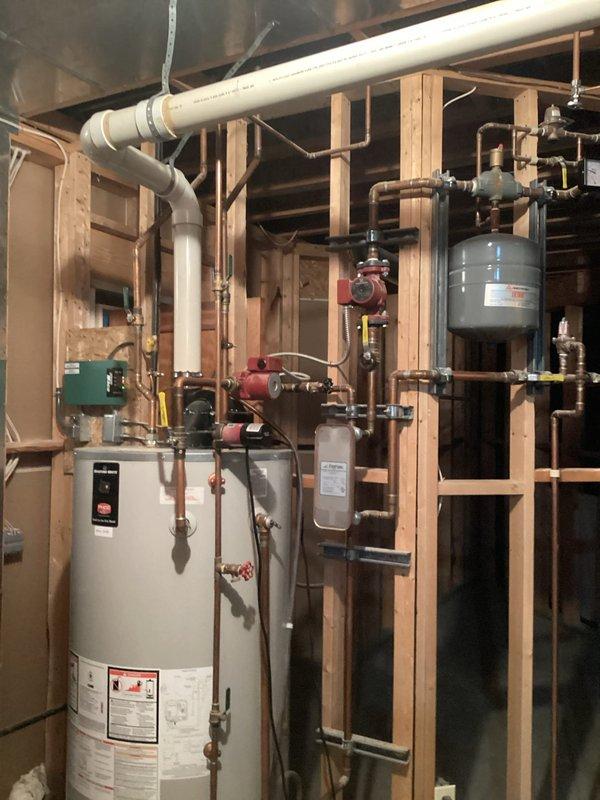 Completed annual cooling system maintenance and inspection. Documented mechanical room installation showing hydronic heating components, circulation pumps, expansion tanks, and copper piping distribution system in unfinished space with exposed framing. All photographed equipment and connections verified for proper operation and accessibility.