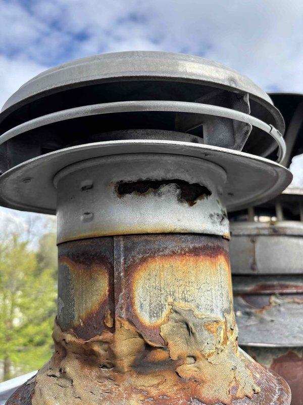 Completed HVAC venting repair work in basement utility area involving furnace ductwork system. Addressed severely corroded chimney cap and vent component showing extensive rust deterioration and paint failure on exterior rooftop installation.
