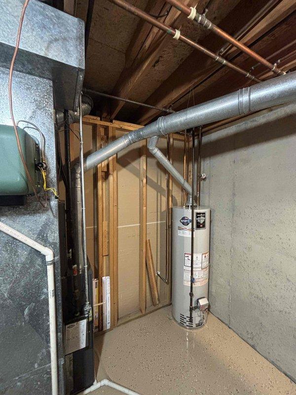 Conducted on-site assessment of existing Bradford White Defender water heater installation in residential basement utility room. Documented current equipment configuration including gas connections, copper supply lines, black iron gas piping, flue venting system, and surrounding mechanical infrastructure. Photographed water heater condition, pipe routing, electrical panel proximity, HVAC ductwork clearances, and overall installation environment to prepare comprehensive replacement estimate.