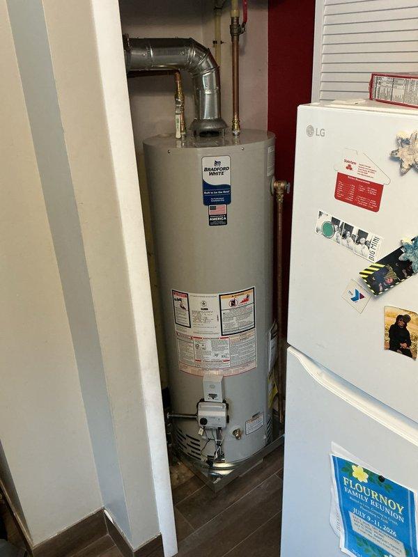 Completed installation of 40-gallon natural gas water heater with short configuration and chimney liner venting system in upper unit utility closet. Repositioned refrigerator to access installation area, installed new water heater with proper venting components including galvanized ductwork, elbow connections, and metal clamps to ensure code-compliant exhaust ventilation. All gas connections, pressure relief valve, and brass fittings were installed and tested for proper operation and safety compliance.