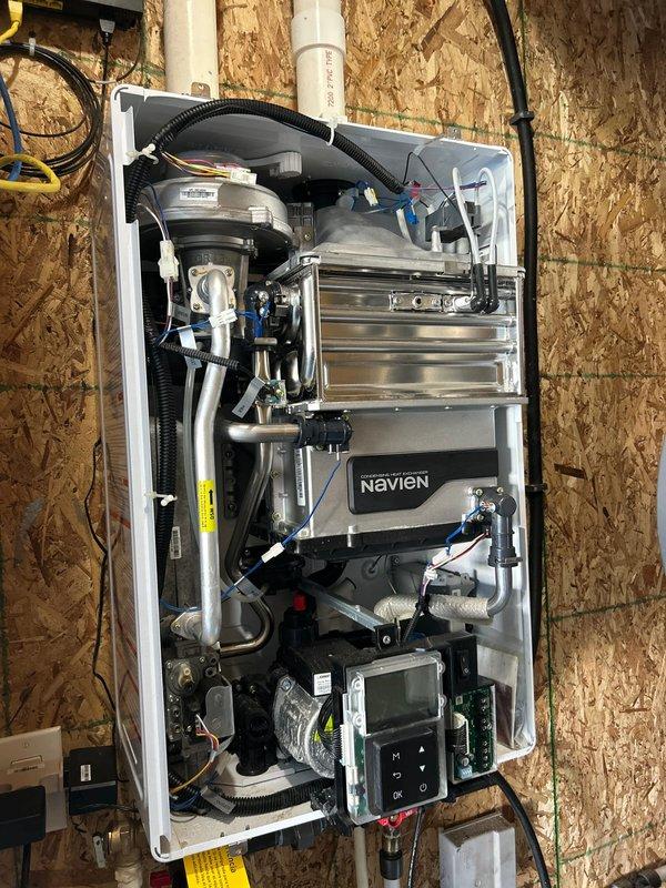 Performed comprehensive tune-up service on Navien tankless water heater unit. Removed front access panel to inspect internal components including heat exchanger, piping connections, and control board. Removed and cleaned inlet filter screen which showed significant debris accumulation and discoloration. Inspected all plumbing connections, drainage hoses, and wiring harnesses for proper operation. Verified digital control panel functionality and system settings. Unit returned to normal operating condition with improved water flow performance.