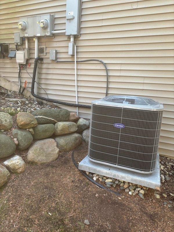 Completed full air conditioning system replacement at residential property. Installed new Carrier condenser unit on concrete pad with proper elevation and stone surround, ran refrigerant lines along exterior wall with secure fastening, and charged system with 5.3 lbs of compressor oil per manufacturer specifications. All electrical connections, disconnect box, and line sets properly installed and tested for optimal system performance.