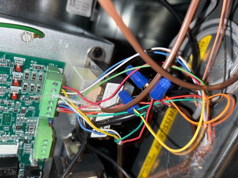 Responded to service call for home experiencing inconsistent heating and cooling performance requiring frequent thermostat adjustments. Upon inspection, found improperly configured thermostat wiring at the wall unit with multiple wire connections requiring verification at the terminal block. Removed thermostat cover to access RC, RH, Y, G, and C terminal connections and traced wiring back to the air handler control board. Inspected the main control board PCB with LED indicators and verified proper voltage at all connection terminals. Examined wire bundle routing between thermostat and HVAC system components, including connections to capacitors and refrigerant line assembly. Corrected thermostat wiring configuration to ensure proper communication between control systems. Verified all terminal connections were secure at both the wall unit and control board. Cycled system through heating and cooling modes to confirm proper operation and stable temperature control without requiring manual 