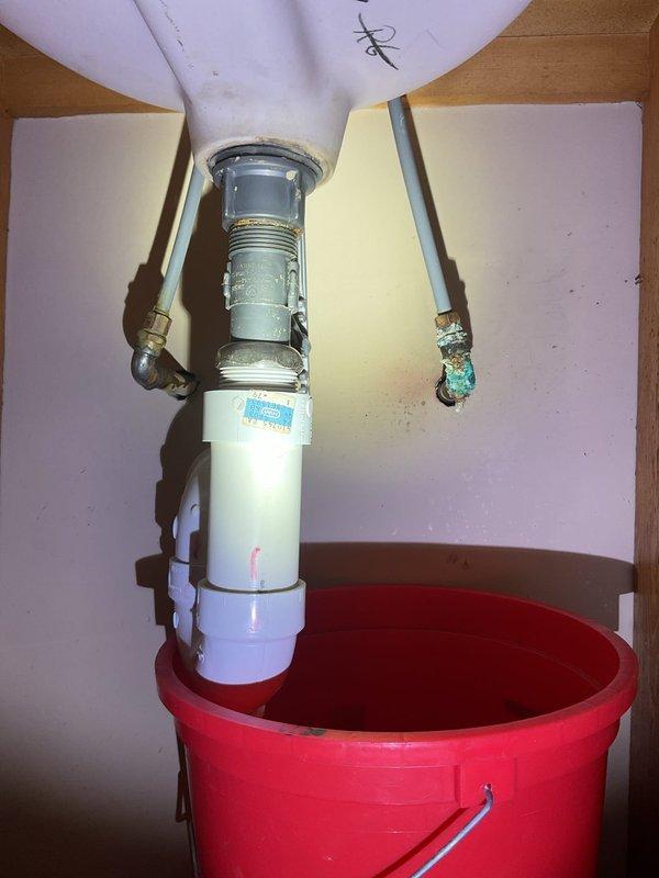 Responded to plumbing leak at residential bathroom sink. Upon inspection, identified two primary issues: deteriorated drain assembly and corroded water supply line with active leak. The chrome sink strainer and drain tailpiece showed wear and required replacement. The copper-colored flexible supply line exhibited significant verdigris corrosion at the lower connection point, causing water seepage. Positioned collection bucket under cabinet to prevent water damage during assessment. Replaced sink drain assembly including new strainer, tailpiece, and P-trap connections with white PVC components. Installed new flexible water supply line to eliminate leak at corroded fitting. Tested all connections for proper seal and verified no additional leaks present. System restored to full functionality with all fixtures operating properly.