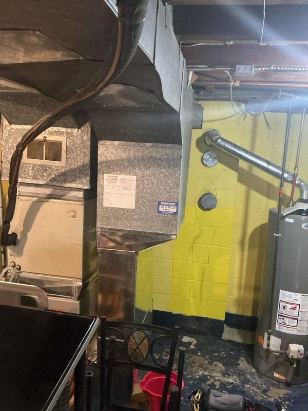 Responded to water heater leak complaint on 12-year-old State brand unit. Upon inspection, confirmed active leak at base of water heater with visible water damage and staining on concrete floor beneath unit. Documented conditions with photographs showing water heater location in basement utility area alongside furnace and HVAC equipment. Customer contacted to discuss replacement options given age of unit and extent of leak.