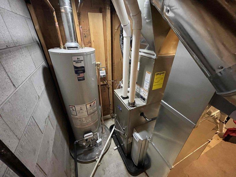 Completed full HVAC and water heating system installation in residential basement utility area. Installed new gas furnace with PVC intake and exhaust venting system, air conditioning unit, and white cylindrical water heater with copper supply connections and control assembly. All equipment properly positioned, vented, and connected according to manufacturer specifications and local code requirements. Exterior penetrations sealed with appropriate utility cover plates on building siding. All systems tested and verified operational upon completion.