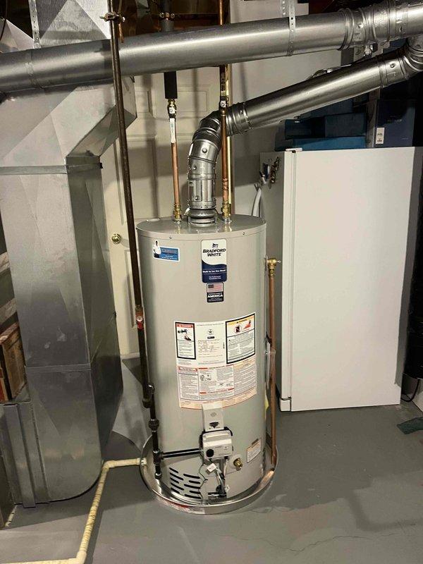 Completed full water heater replacement in basement utility room. Installed new residential tank-style water heater with proper venting through black flue pipe and connected all copper supply lines to existing plumbing system. Mounted blue expansion tank on wall with appropriate piping connections and integrated shutoff valves for system isolation and maintenance access. All connections tested and verified operational.