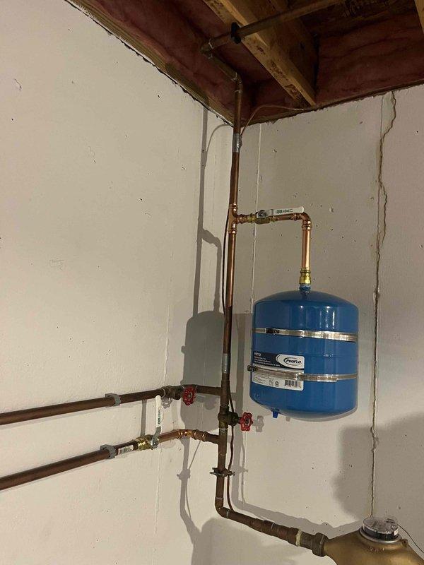Completed full water heater replacement in basement utility room. Installed new residential tank-style water heater with proper venting through black flue pipe and connected all copper supply lines to existing plumbing system. Mounted blue expansion tank on wall with appropriate piping connections and integrated shutoff valves for system isolation and maintenance access. All connections tested and verified operational.