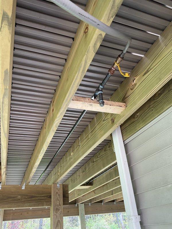 Completed gas line installation and routing for residential deck structure. Installed and secured new gas piping along deck fascia and through underside of covered porch area, utilizing pressure-treated lumber support system for proper mounting. Employed ratchet straps for temporary stabilization during installation process. Routed gas line in compliance with code requirements, ensuring proper clearances from electrical conduit and maintaining secure attachment points to structural beams. All connections tested and verified for safe operation.
