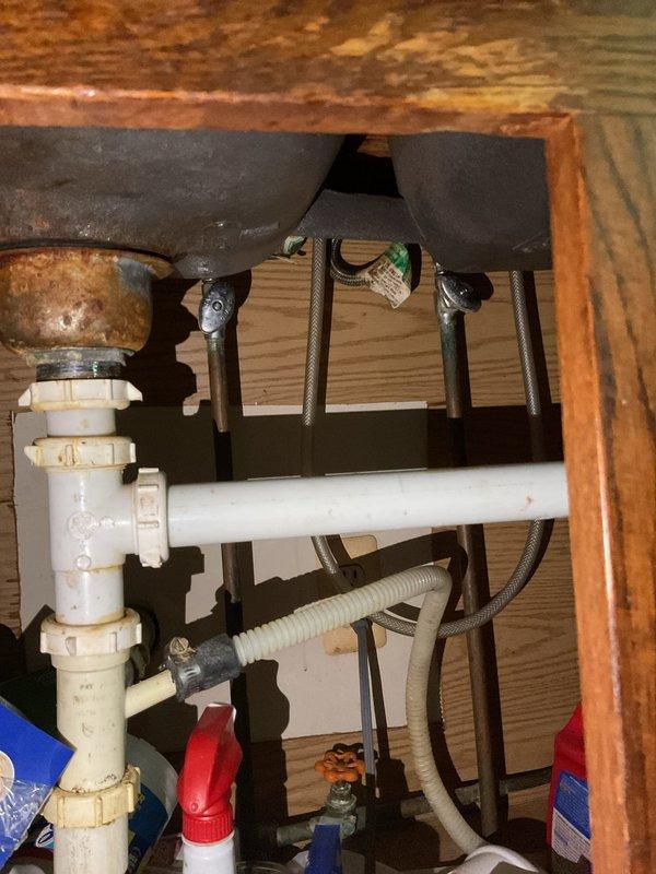 Completed comprehensive plumbing inspection of two adjacent residential units, examining all faucets, fixtures, and supply lines for potential leaks or deficiencies. Kitchen inspection revealed functional chrome gooseneck faucet with double-basin sink in satisfactory condition. Under-sink cabinet inspection identified corroded metal drain piping showing significant rust and deterioration requiring attention, with PVC P-trap assembly and braided flexible supply lines otherwise intact. All visible plumbing fixtures and connections were evaluated for proper operation and leak detection across both properties.