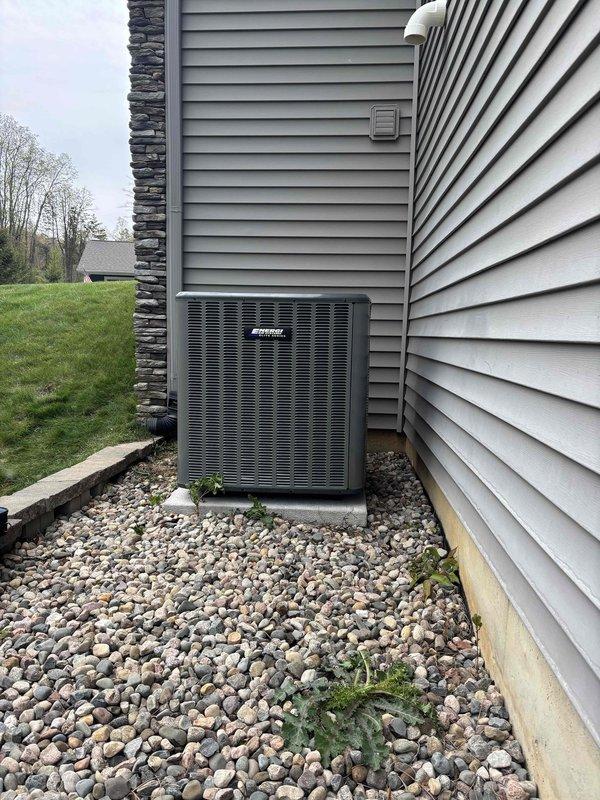 Completed full air conditioning system replacement at residential property. Removed existing outdoor condensing unit and installed new AC unit on concrete pad against exterior wall with proper electrical disconnect and conduit installation. Unit positioned on white concrete pad with surrounding river rock landscaping, ensuring proper clearances and drainage for optimal system performance.
