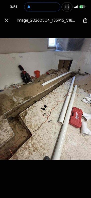 Completed drain work and clean waste/overflow installation in active construction area. Installed white PVC drainage piping through floor joists and subflooring, routing lines diagonally across joist cavities to accommodate proper pitch and connection points. Work performed in unfinished space with exposed framing, requiring coordination with ongoing construction activities and protection of surrounding areas.