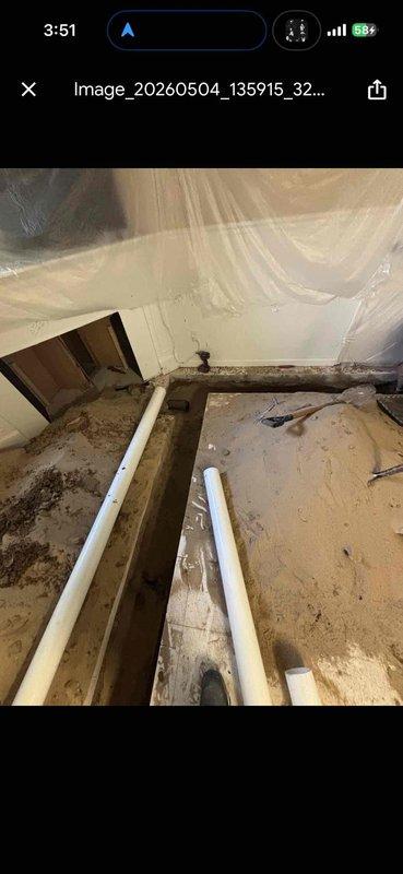 Completed drain work and clean waste/overflow installation in active construction area. Installed white PVC drainage piping through floor joists and subflooring, routing lines diagonally across joist cavities to accommodate proper pitch and connection points. Work performed in unfinished space with exposed framing, requiring coordination with ongoing construction activities and protection of surrounding areas.