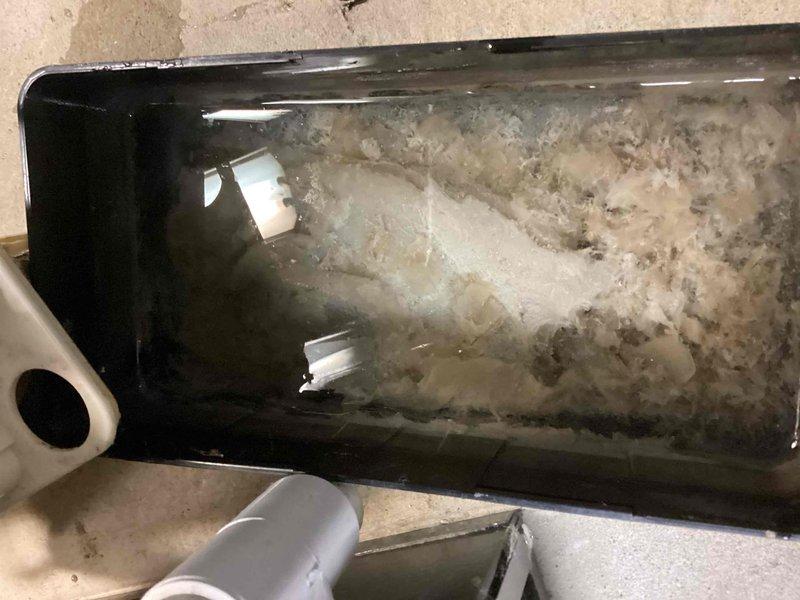 Completed annual cooling system tune-up and inspection. Found condensate drain pan with severe mineral deposit buildup and scale accumulation, indicating prolonged water exposure and lack of maintenance. Documented equipment condition with photos showing extensive white and grayish deposits throughout pan interior, which could lead to drainage issues and potential water damage if left unaddressed.