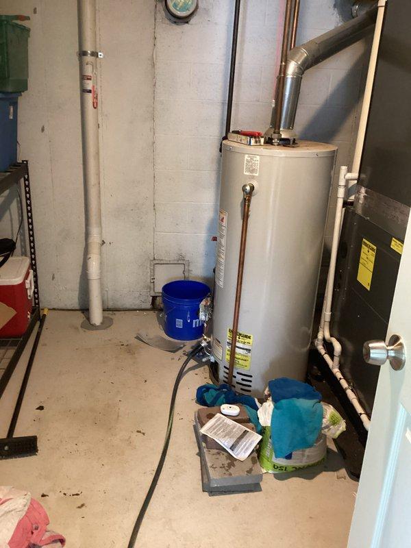 Responded to emergency water leak from 18-year-old Bradford White atmospheric storage water heater actively flooding basement. Upon arrival, confirmed main water supply had been shut off to prevent further water damage. Inspected unit and documented conditions with photographs showing significant water accumulation requiring immediate attention. Assessed water heater age, condition, and leak severity to determine unit had reached end of serviceable life and required replacement rather than repair.