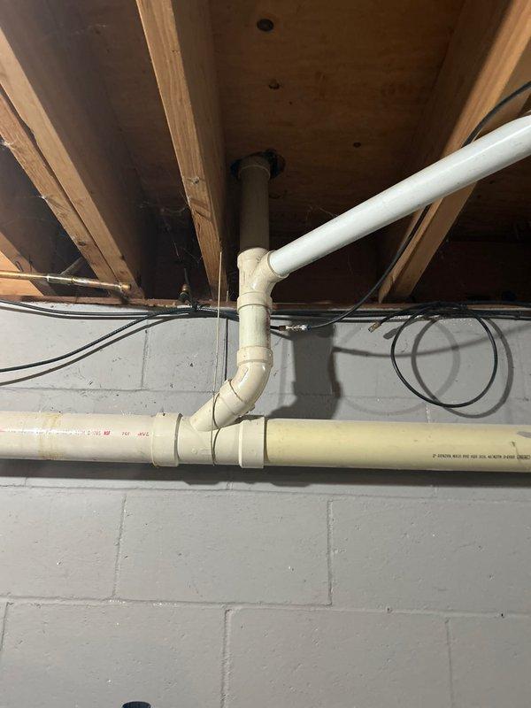 Responded to intermittent dishwasher drain line overflow in basement of 1973-built home. Upon inspection, identified improper drainage routing in exposed PVC piping system running through floor joists. Corrected drain line configuration to eliminate standing water and ensure proper gravity flow, preventing future overflow conditions. System tested successfully with no further drainage issues observed.