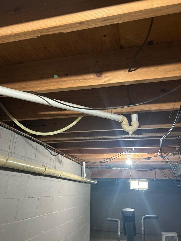 Responded to intermittent dishwasher drain line overflow in basement of 1973-built home. Upon inspection, identified improper drainage routing in exposed PVC piping system running through floor joists. Corrected drain line configuration to eliminate standing water and ensure proper gravity flow, preventing future overflow conditions. System tested successfully with no further drainage issues observed.