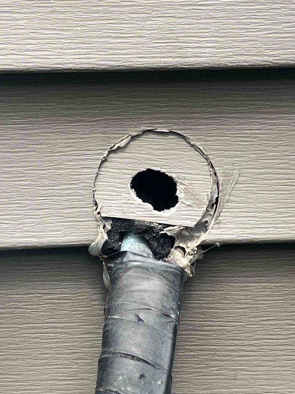 Responded to service call for 15-year-old air conditioning system with multiple concerns including unlevel condenser unit, suspected disconnected refrigerant line, and uneven cooling in one room. Upon arrival, documented extensive overgrowth of vegetation surrounding outdoor condenser unit, which was restricting proper airflow and potentially affecting system efficiency. Inspected exterior exhaust vent and discovered significant damage to galvanized vent pipe with approximately 2-3 inch diameter hole torn through metal wall, exposing interior cavity with visible debris accumulation. Assessed condenser unit positioning and confirmed unit was not level on concrete pad. Evaluated refrigerant lines for disconnection or damage as reported. Investigated temperature imbalance issue affecting specific room to identify potential ductwork, airflow, or zoning problems. Photographed damaged vent pipe showing jagged metal tears and weathering, as well as condenser unit surrounded by tall grass and 