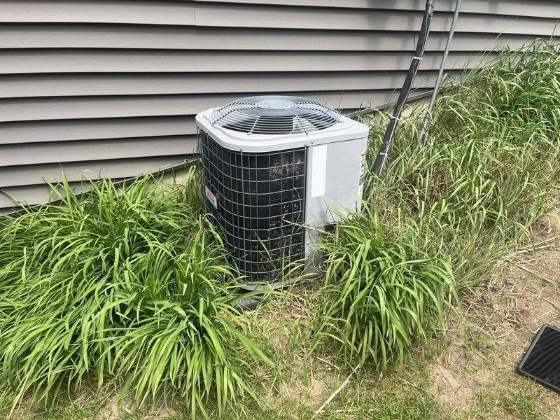 Responded to service call for 15-year-old air conditioning system with multiple concerns including unlevel condenser unit, suspected disconnected refrigerant line, and uneven cooling in one room. Upon arrival, documented extensive overgrowth of vegetation surrounding outdoor condenser unit, which was restricting proper airflow and potentially affecting system efficiency. Inspected exterior exhaust vent and discovered significant damage to galvanized vent pipe with approximately 2-3 inch diameter hole torn through metal wall, exposing interior cavity with visible debris accumulation. Assessed condenser unit positioning and confirmed unit was not level on concrete pad. Evaluated refrigerant lines for disconnection or damage as reported. Investigated temperature imbalance issue affecting specific room to identify potential ductwork, airflow, or zoning problems. Photographed damaged vent pipe showing jagged metal tears and weathering, as well as condenser unit surrounded by tall grass and 