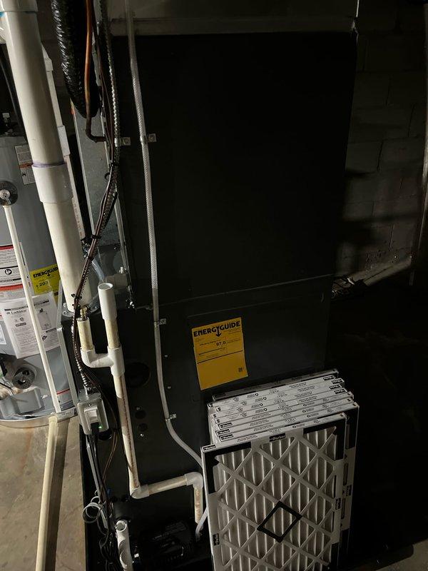 Completed full HVAC system replacement including new furnace and air conditioning unit in basement utility area. Installed black vertical air handler with pleated air filter, connected all necessary PVC condensate drainage lines, refrigerant lines, and electrical connections per manufacturer specifications. System tested and verified operational with all safety controls functioning properly.