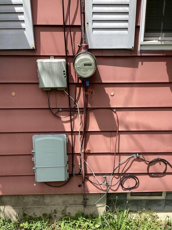 Completed electrical estimate for panel upgrade at 73-year-old residential property. Evaluated existing exterior electrical service equipment including digital meter, junction box, and main panel mounted on exterior wall with multiple conduits and service entrance conductors. Assessed interior basement electrical installation featuring main service panel and disconnect switch mounted on wooden board against concrete block wall. Documented current electrical infrastructure condition, wire sizing, panel capacity, and service entrance configuration. Photographed both exterior meter base assembly and interior panel arrangement to provide comprehensive assessment for recommended 200-amp service upgrade to meet modern electrical code requirements and household power demands.