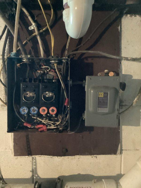 Completed electrical estimate for panel upgrade at 73-year-old residential property. Evaluated existing exterior electrical service equipment including digital meter, junction box, and main panel mounted on exterior wall with multiple conduits and service entrance conductors. Assessed interior basement electrical installation featuring main service panel and disconnect switch mounted on wooden board against concrete block wall. Documented current electrical infrastructure condition, wire sizing, panel capacity, and service entrance configuration. Photographed both exterior meter base assembly and interior panel arrangement to provide comprehensive assessment for recommended 200-amp service upgrade to meet modern electrical code requirements and household power demands.
